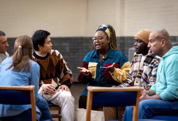 Medium shot of a group of adults sitting in a circle and talking to each other about their mental well-being. They are all wearing casual clothing. The community centre is located in Seaton Deleval in the North East of England.