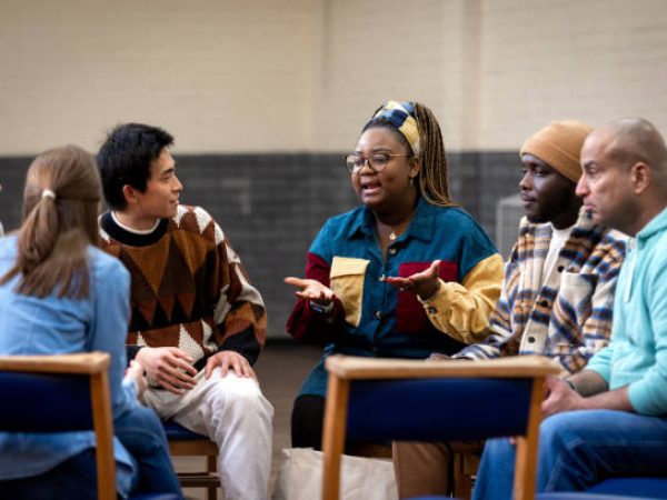 Medium shot of a group of adults sitting in a circle and talking to each other about their mental well-being. They are all wearing casual clothing. The community centre is located in Seaton Deleval in the North East of England.